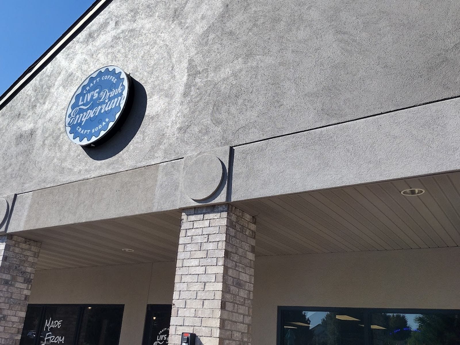 Exterior of Liv's Drink Emporium with a round blue sign above brick columns on a sunny day.