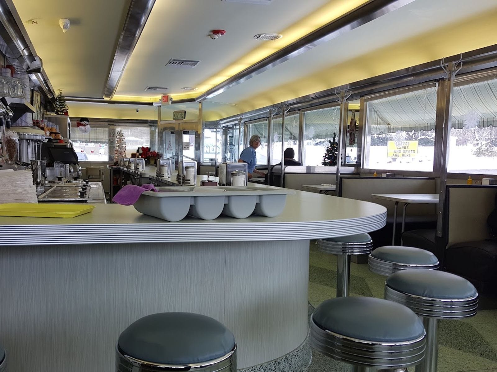 Retro diner interior with chrome stools, counter, booths, and holiday decorations in the windows.