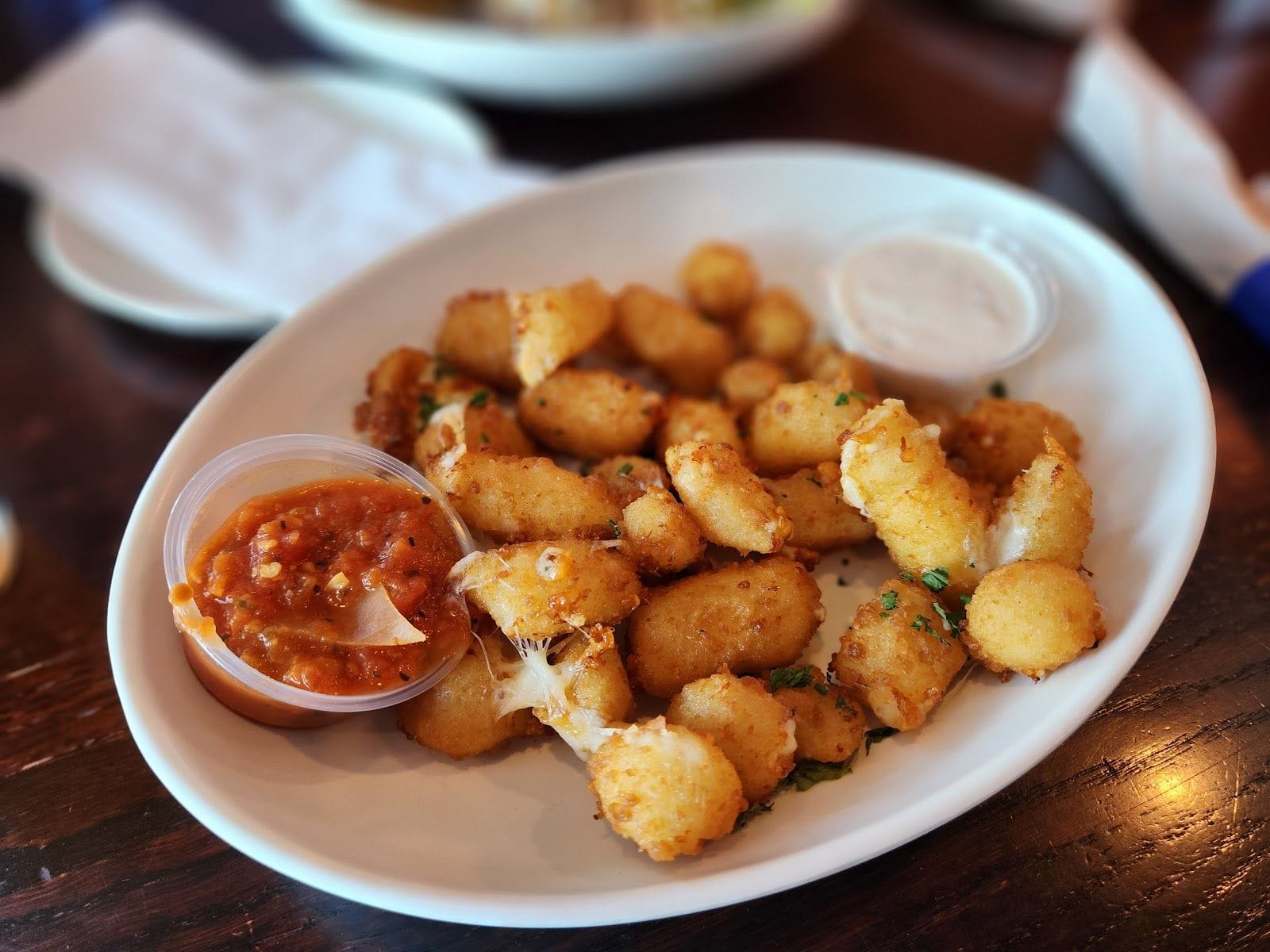 Plate of golden fried cheese curds with marinara and ranch dipping sauces on a wooden table.