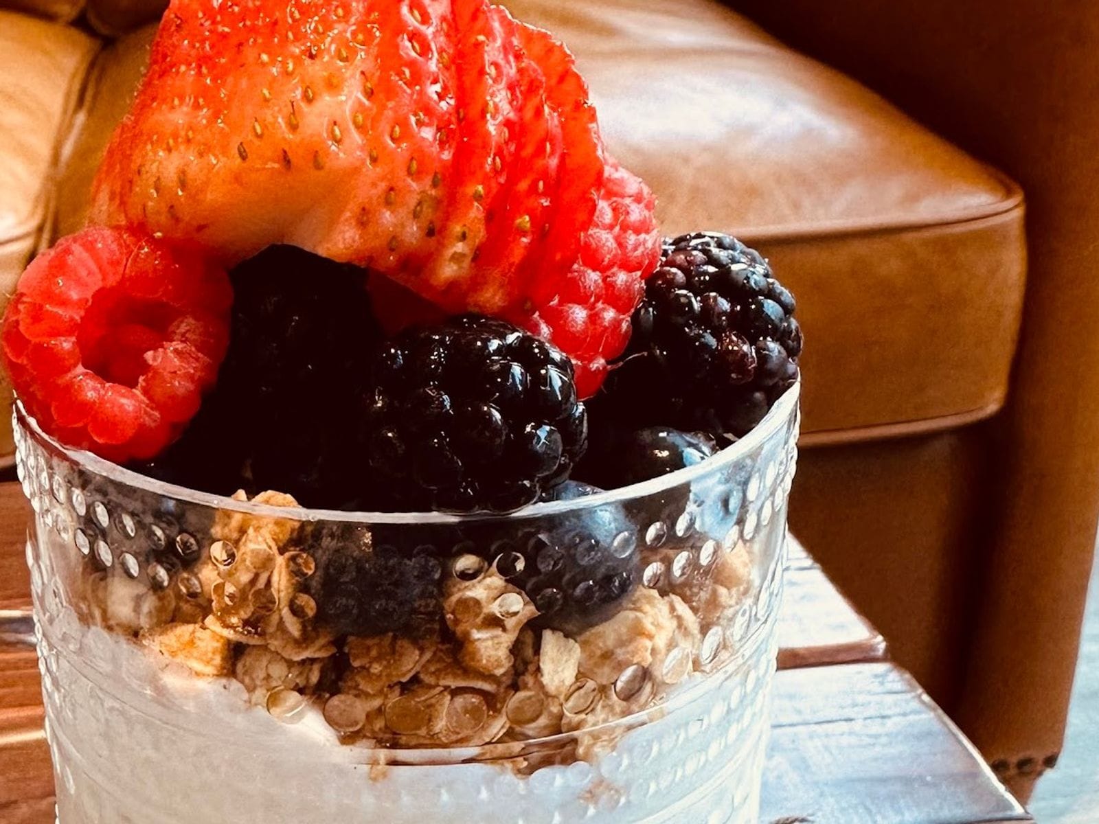 Glass cup filled with granola, yogurt, strawberries, raspberries, and blackberries on a wooden table.
