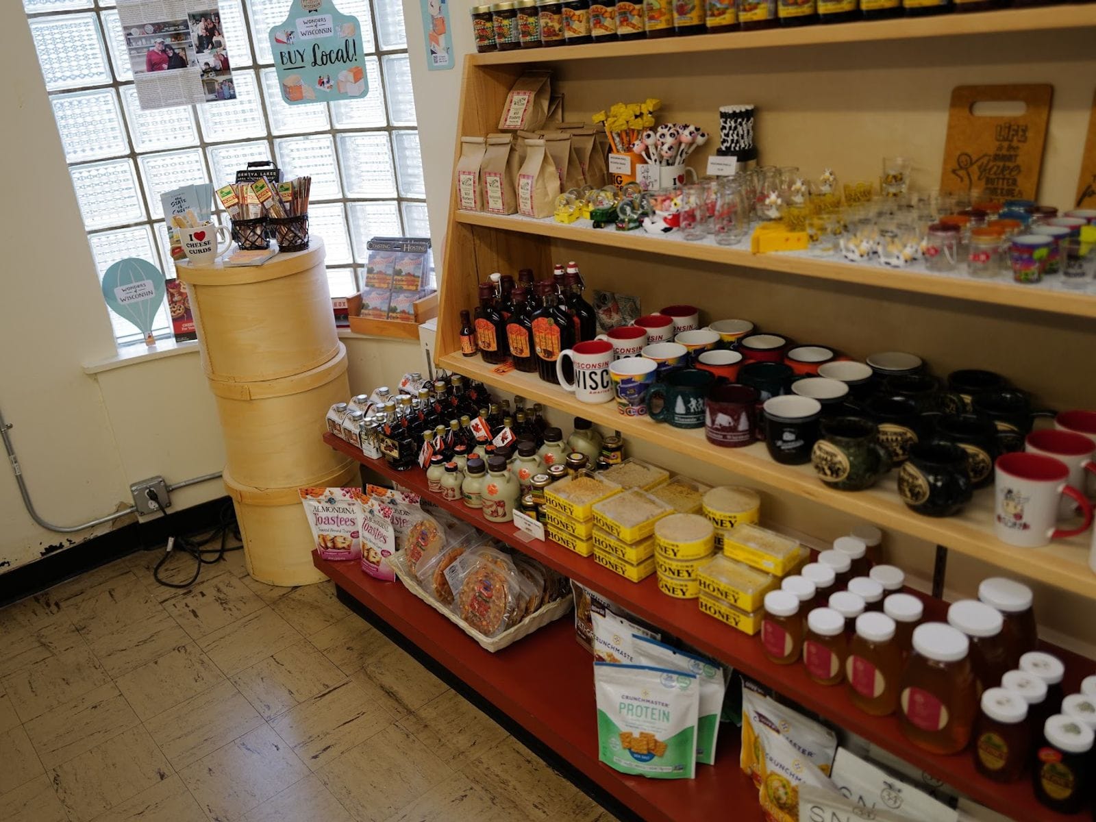 Shelves filled with mugs, honey, syrup, snacks, and Wisconsin-themed souvenirs in a small shop corner.