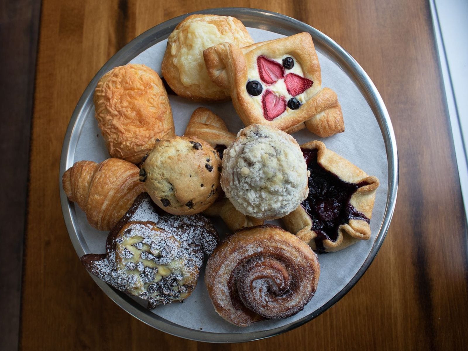 Assorted pastries including croissants, muffins, and fruit danishes on a round metal tray at Marquette Cafe.