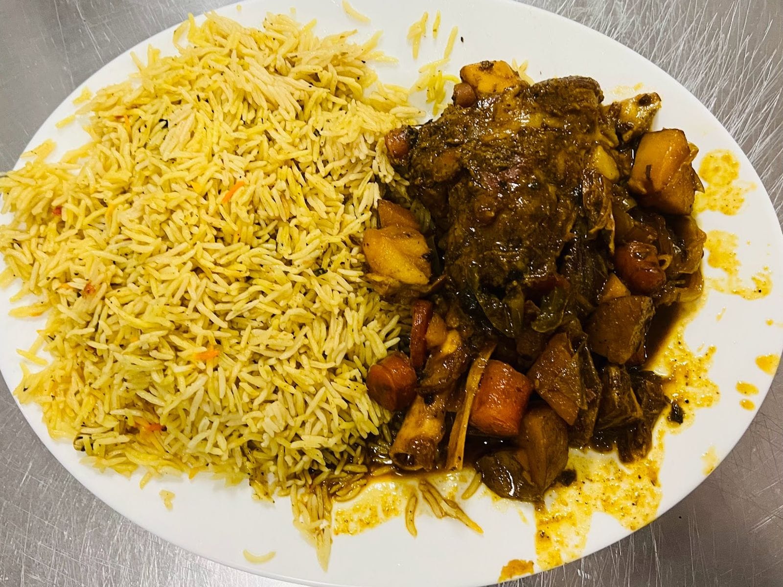 Oval plate with yellow rice and a hearty serving of stew with meat and vegetables.