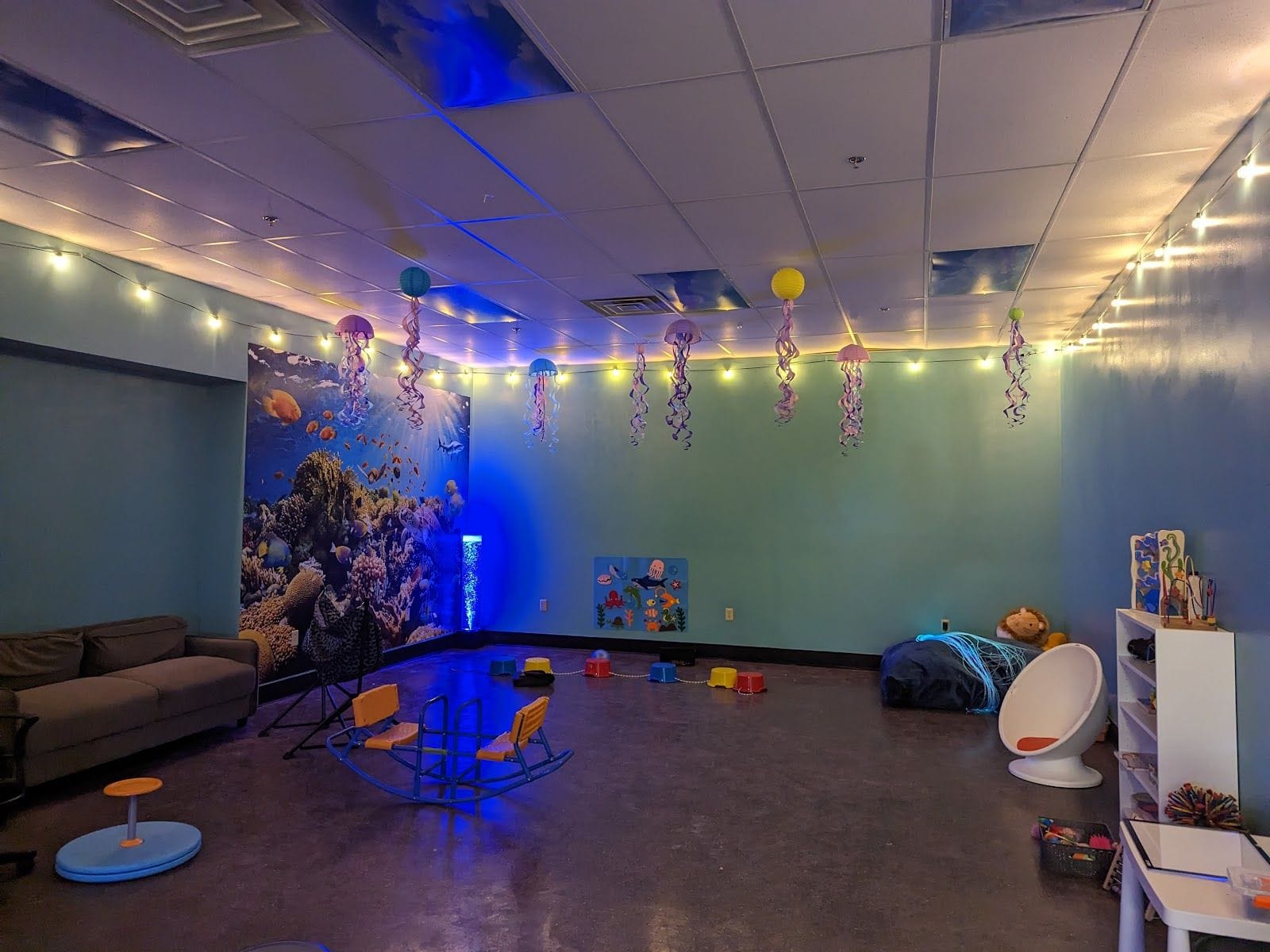 Colorful indoor sensory playroom with adaptive equipment, ocean mural, and twinkling ceiling lights.