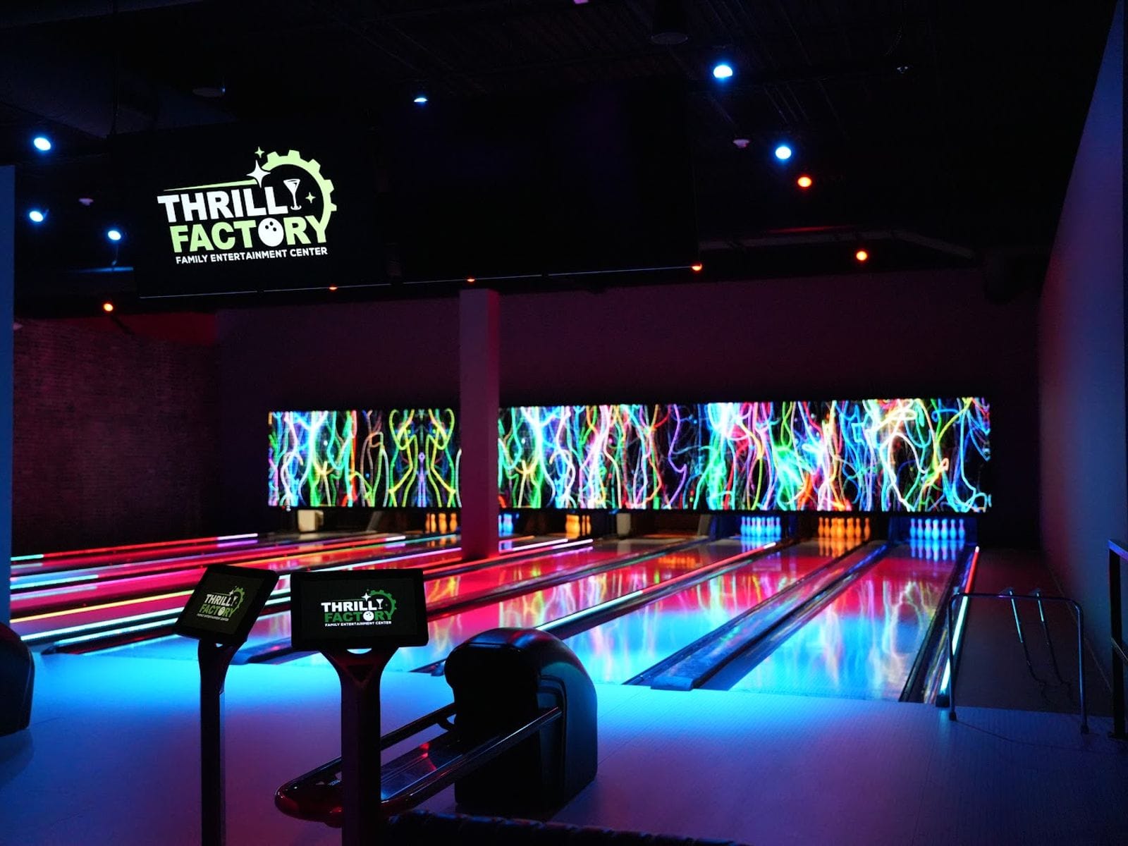 Neon-lit bowling lanes at Thrill Factory Entertainment with vibrant, colorful wall displays.