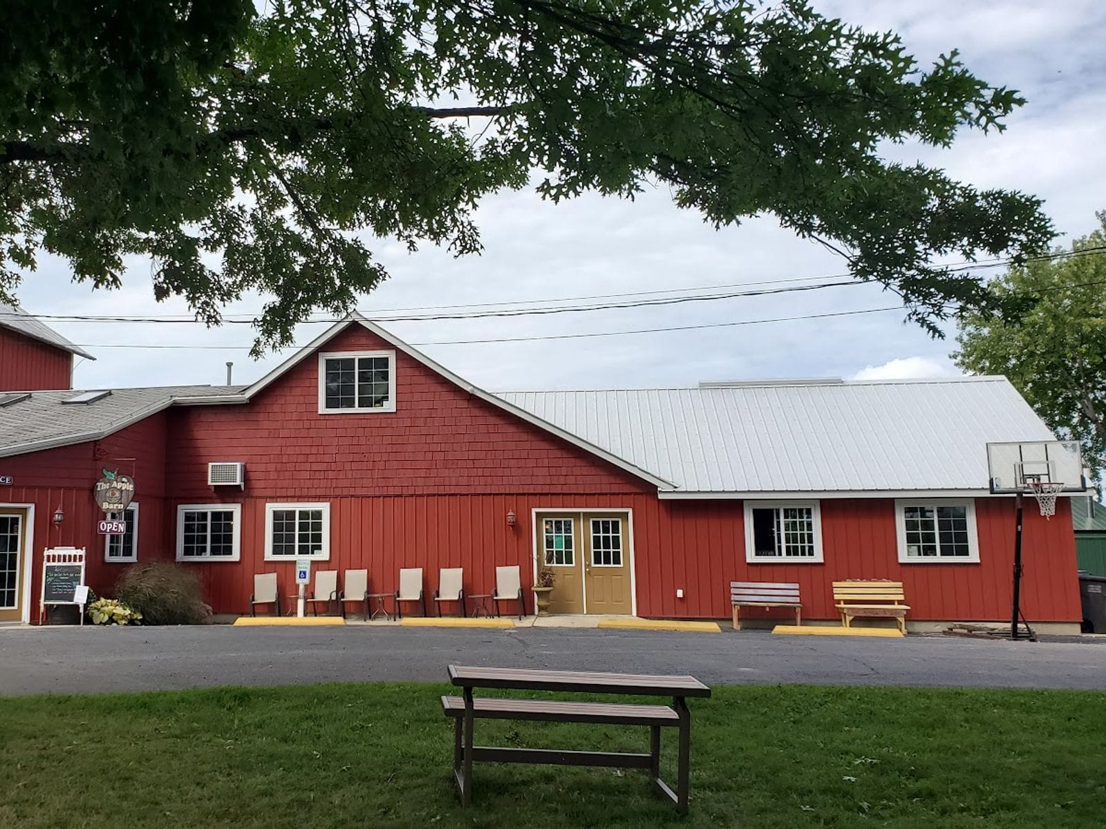 Red barn-style building with white trim, benches, and picnic table under leafy trees.