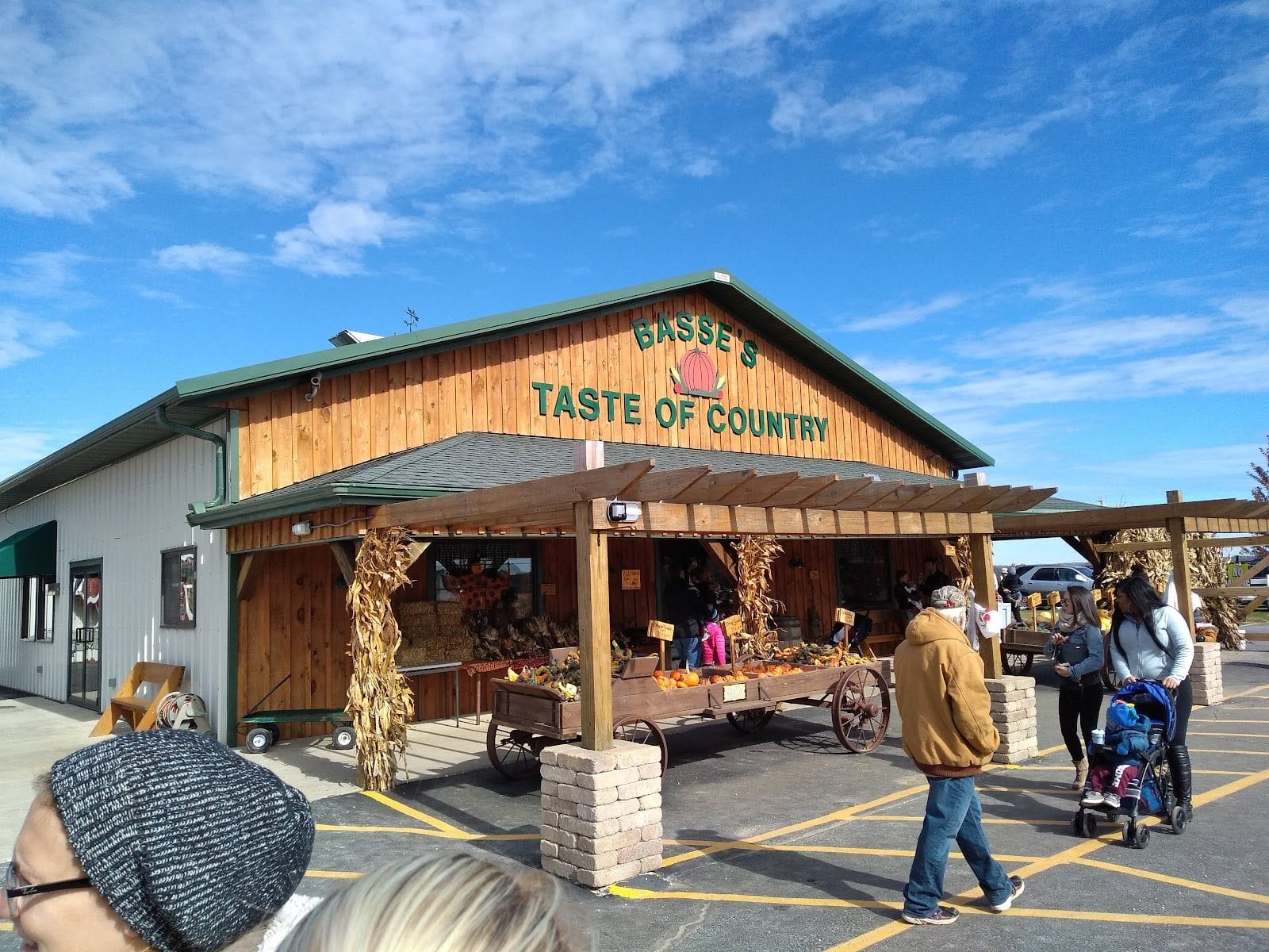 People gather outside Basse's Taste of Country farm stand decorated with autumn produce and cornstalks.