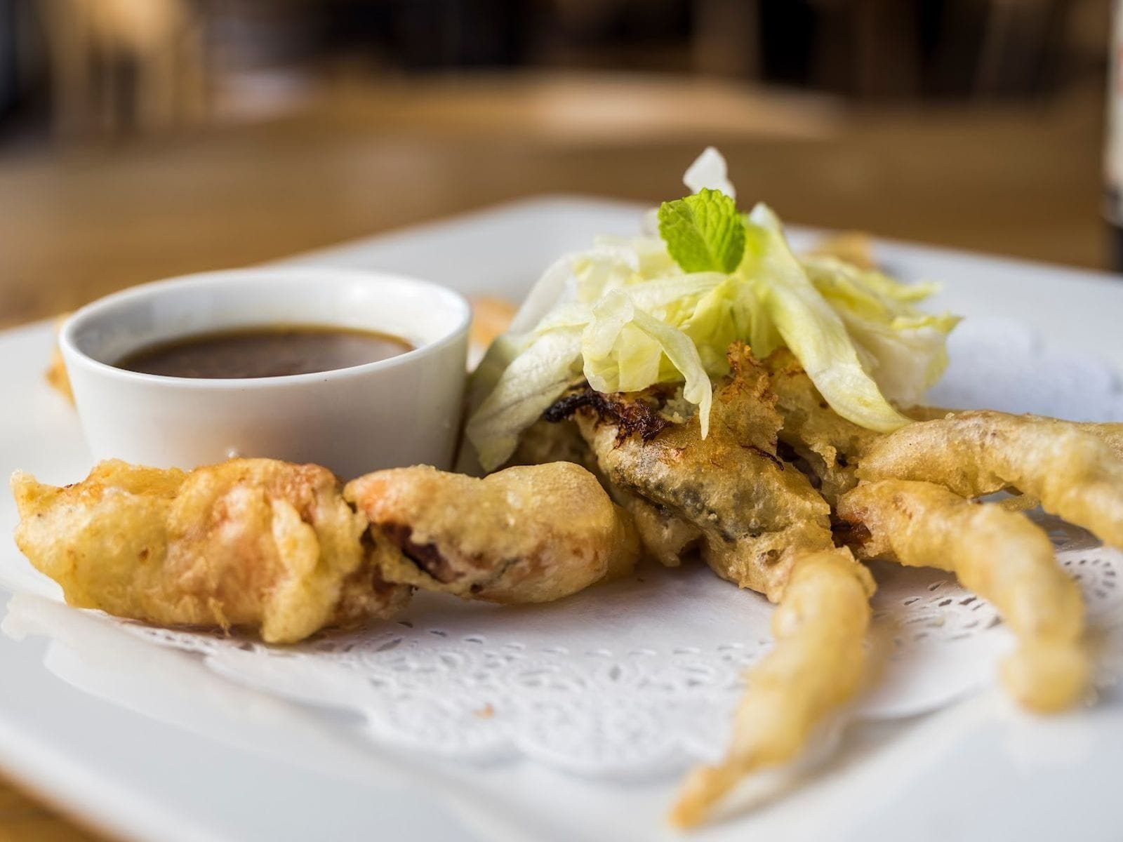 Close-up of golden tempura pieces with dipping sauce and shredded lettuce on a white plate.