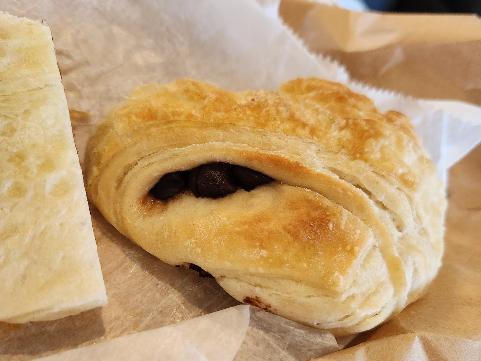 Flaky pain au chocolat pastry with visible chocolate filling on parchment paper.