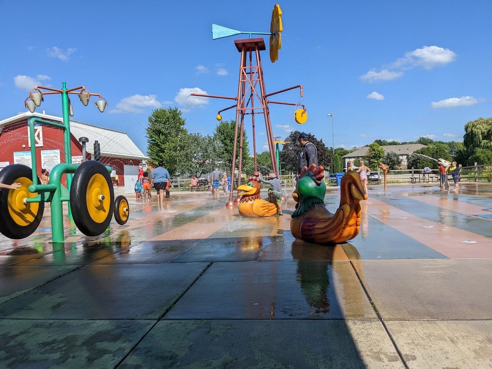 Children play in a colorful farm-themed splash pad with animal sculptures at McKee Farms Park.