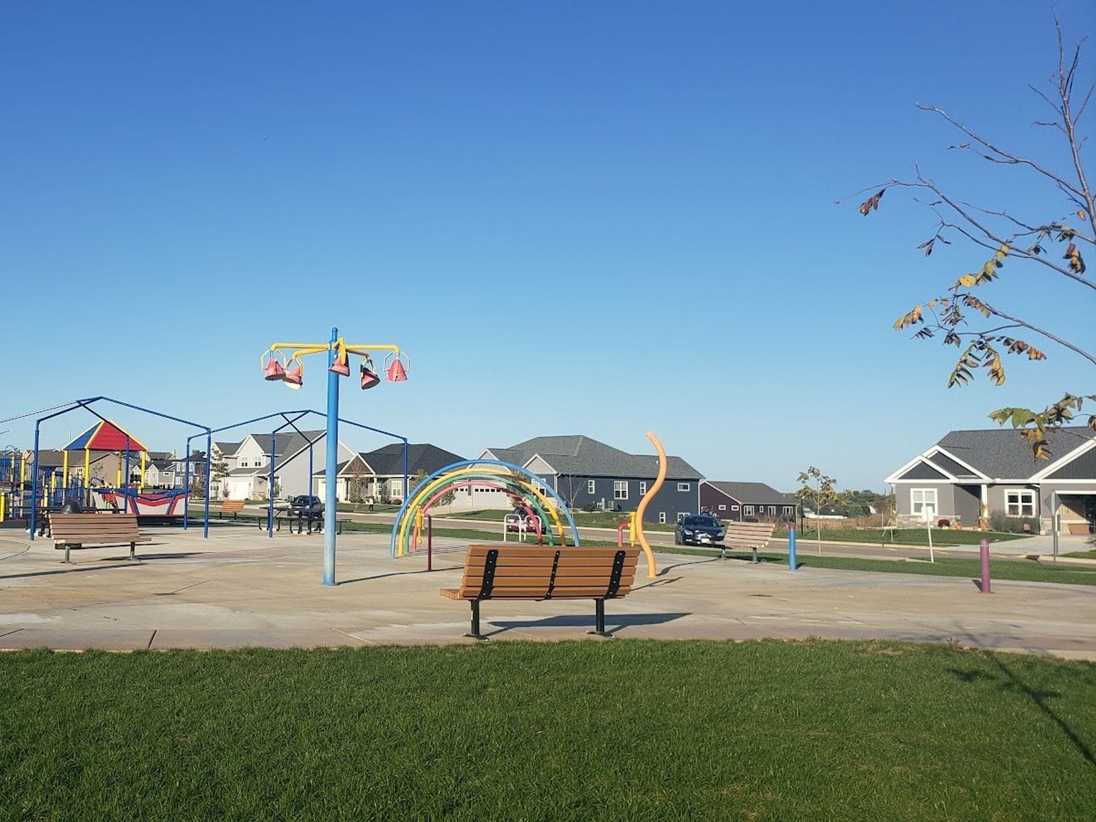 Colorful splash pad and playground at Nordic Ridge Park with benches and nearby houses under a clear sky.
