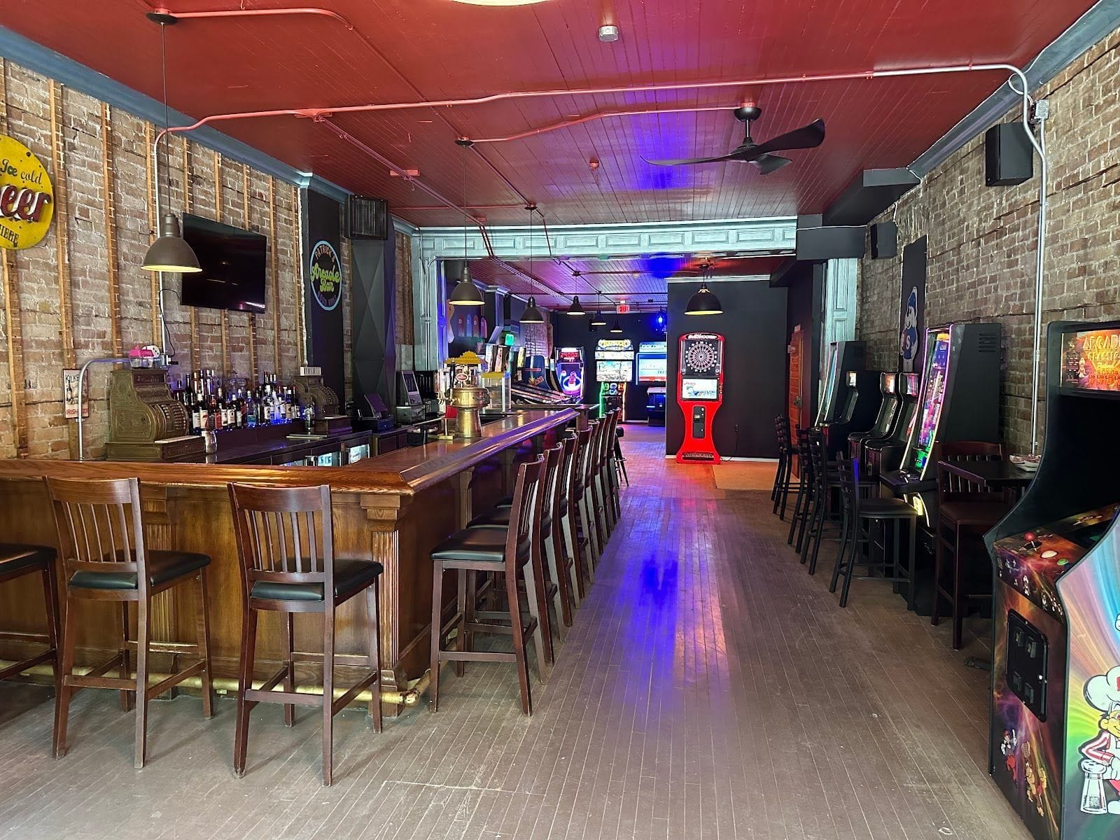 Cozy bar with wooden stools, arcade machines, dartboard, and neon lights at Patrick’s Arcade Bar.