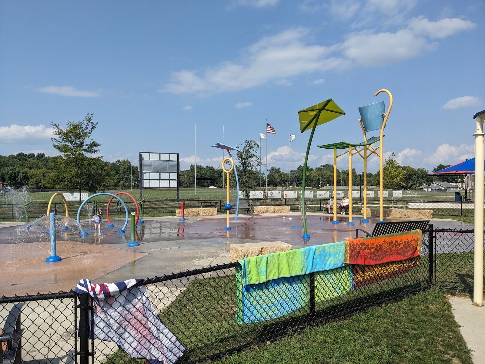 Colorful splash pad with water features and towels on a fence at Phoebe Bakken Memorial Park.