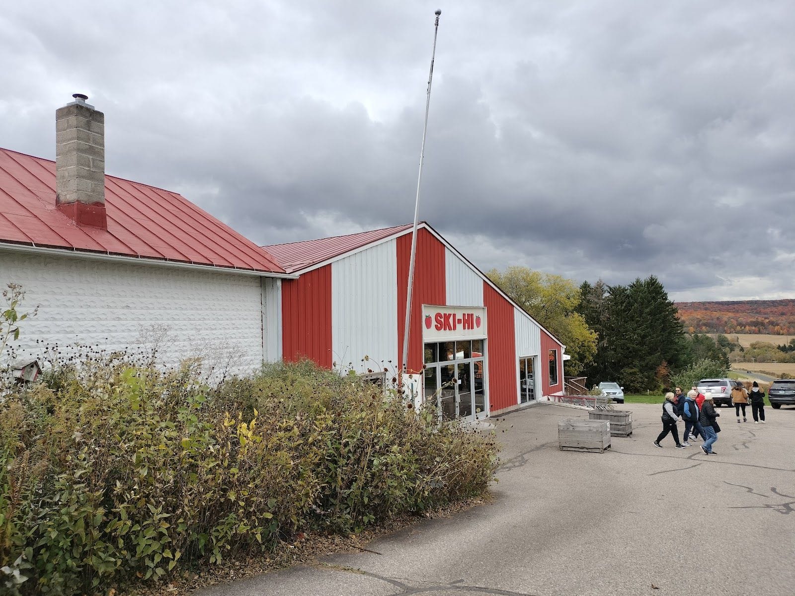 People walk toward the red and white Ski-Hi Fruit Farm building under a cloudy autumn sky.