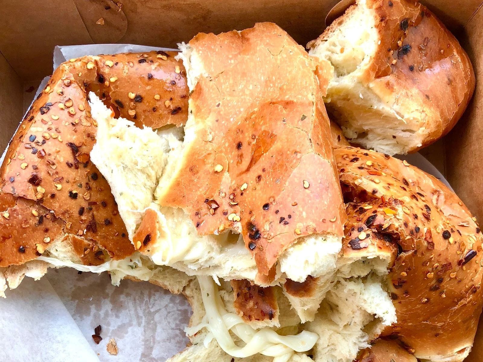 Torn pieces of golden bread topped with red pepper flakes and melted cheese inside a bakery box.