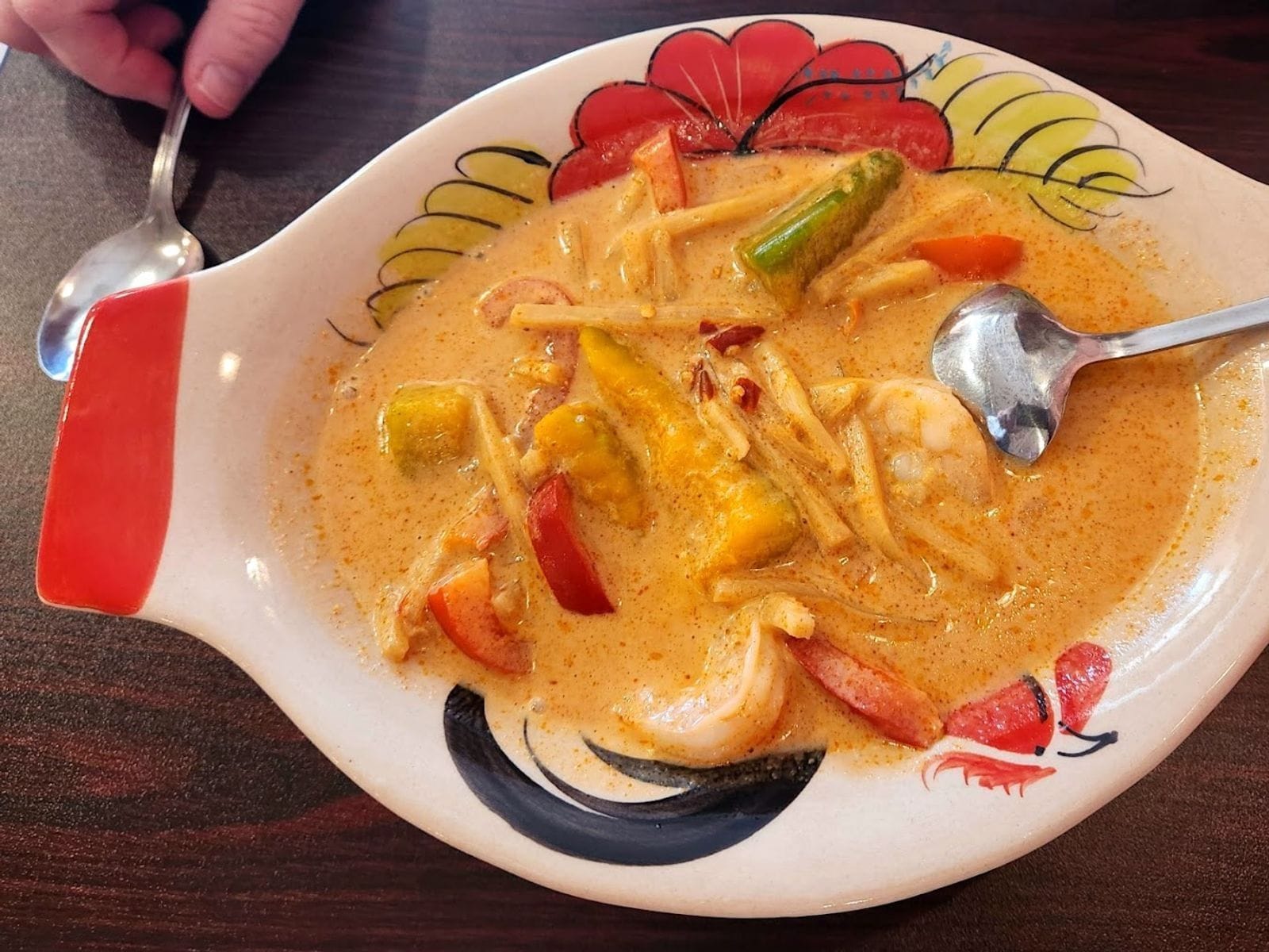 Bowl of Thai curry soup with shrimp, veggies, and noodles in a decorative dish on a wooden table.