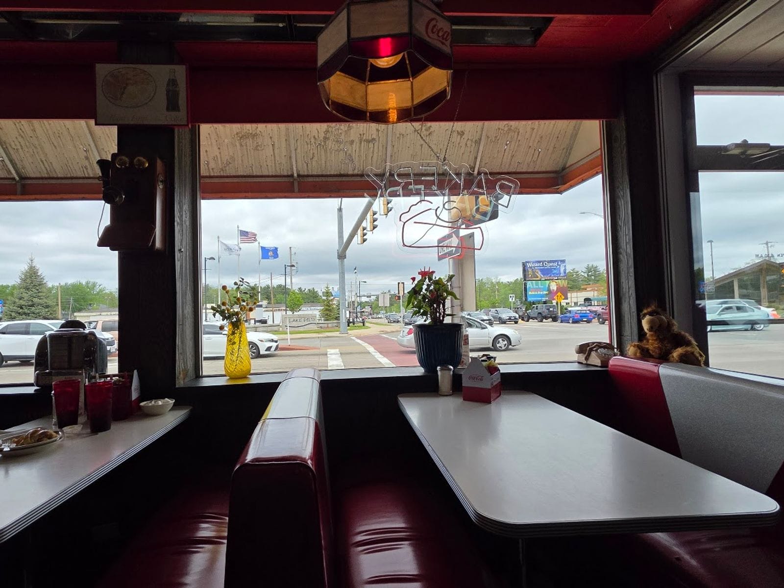 Cozy red diner booth with flowers and stuffed animal by large windows, overlooking a busy street.