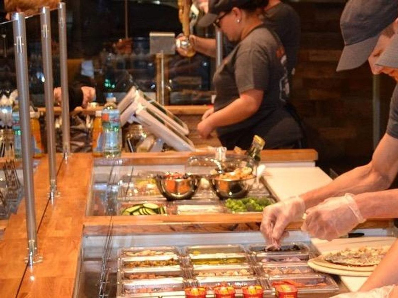 Staff preparing custom pizzas behind a glass counter filled with fresh toppings at Dells Pizza Lab.