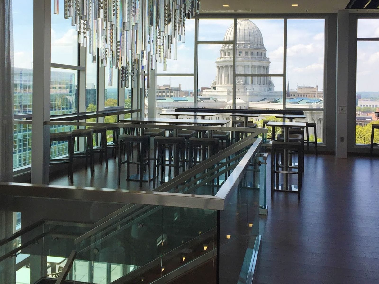 Sleek dining area with tall tables, glass chandeliers, and panoramic city views of a domed building.