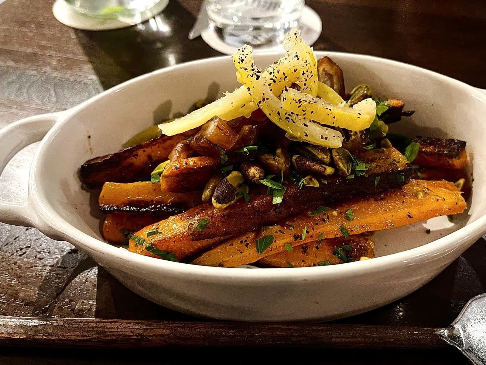Roasted carrots topped with herbs, nuts, and thinly sliced vegetables in a white ceramic dish.