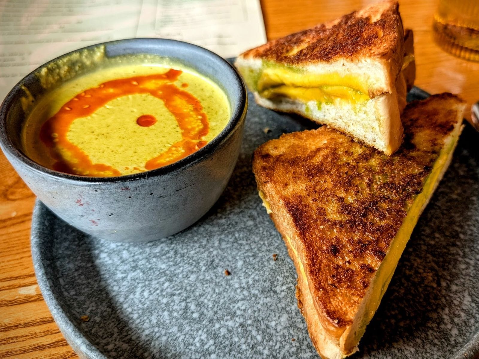 Grilled cheese sandwich halves on a plate beside a bowl of creamy soup topped with orange oil swirl.