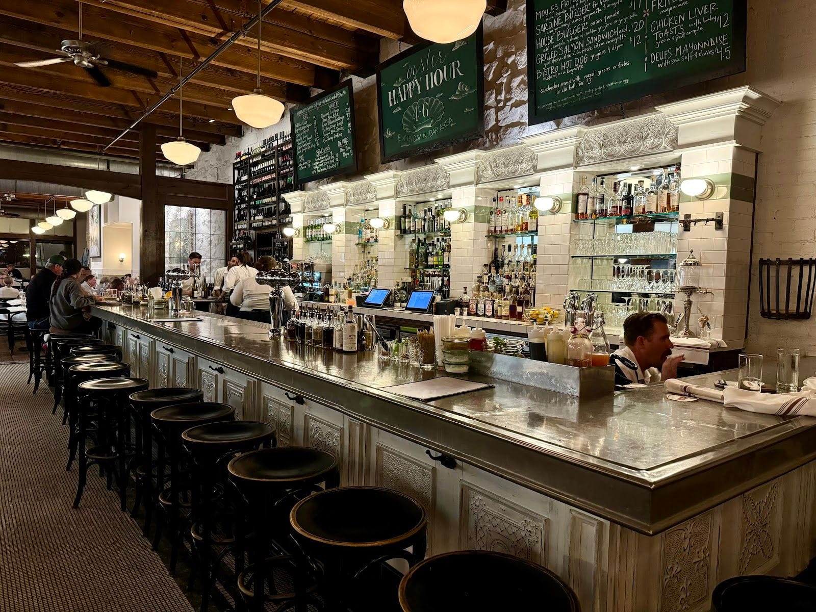 Elegant wine bar with a long marble counter, black stools, and shelves of bottles behind the bar.