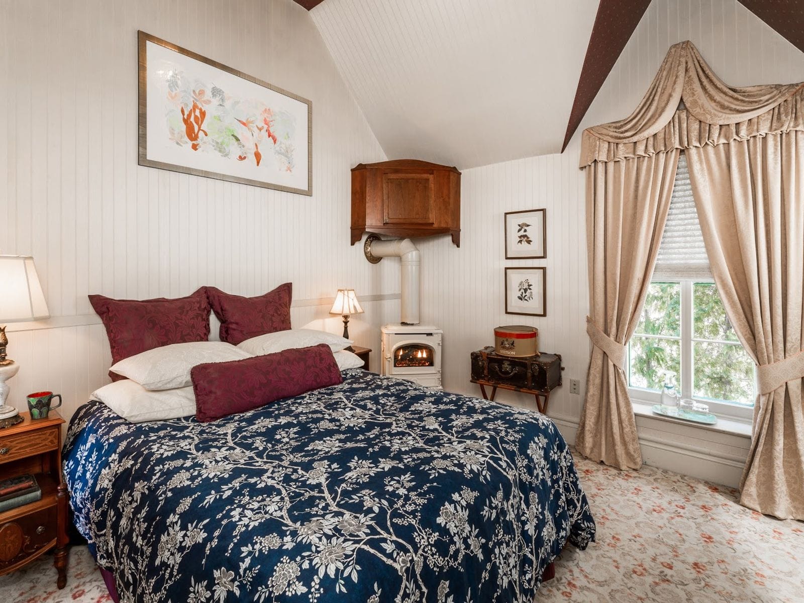 Elegant bedroom with floral bedding, vintage stove, ornate drapes, and classic furnishings.