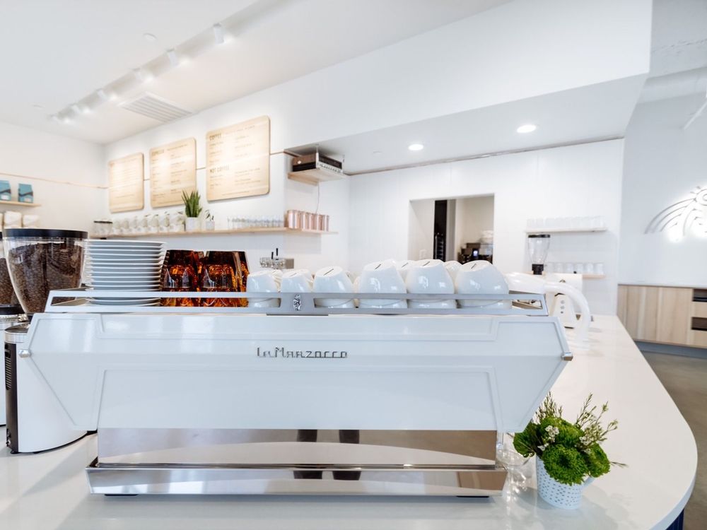 Sleek white espresso machine with stacked cups on a bright, sunlit café counter at Wonderstate Coffee.