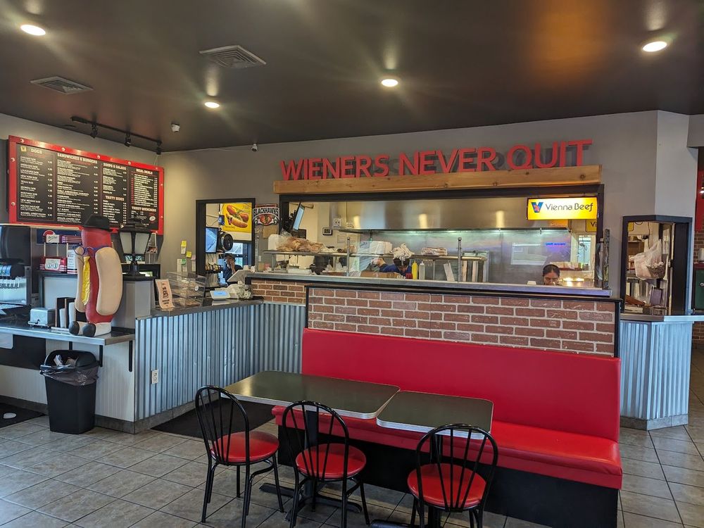 Casual diner with red booths, a hot dog statue, and a counter under a “Wieners Never Quit” sign.