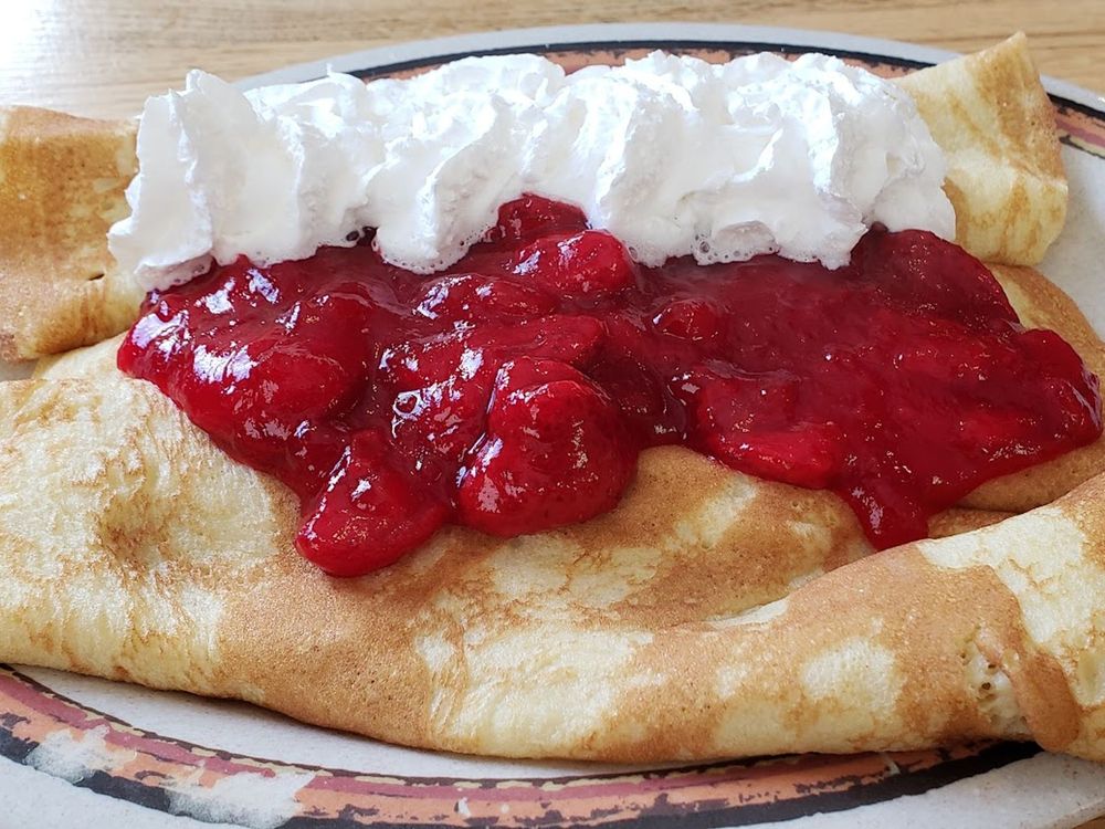 Golden crepes topped with strawberry sauce and a generous swirl of whipped cream on a diner plate.