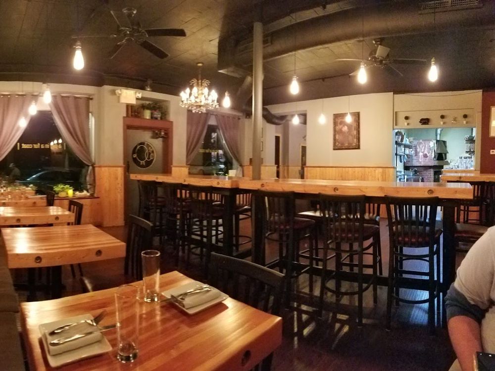 Cozy restaurant interior with wooden tables, black chairs, pendant lights, and mauve curtains.