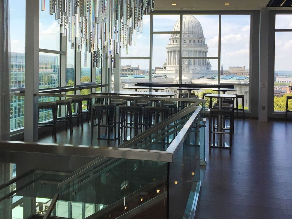 Modern wine bar interior with tall tables, glass walls, and a view of a domed government building outside.