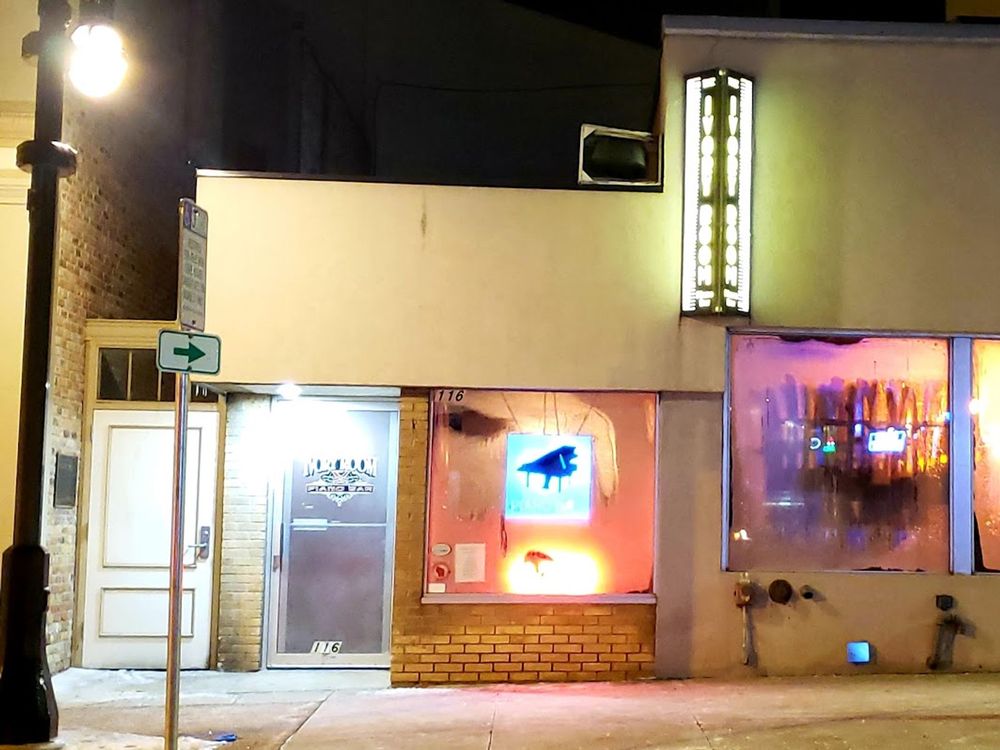 Exterior of Ivory Room Piano Bar at night, featuring neon piano sign and glowing lights in front windows.