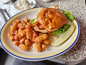 A delicious plate featuring a chicken sandwich with lettuce, fried bites, and a pickle on the side.