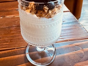 Glass parfait cup filled with creamy yogurt, granola, and berries on a rustic wooden table.