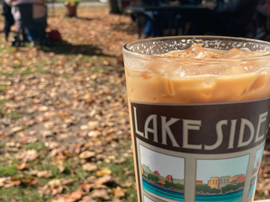 Iced coffee in a Lakeside St. Coffee House cup, held outdoors with autumn leaves scattered on the ground.