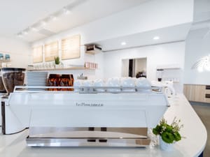 Sleek white espresso machine with stacked cups on a bright, sunlit café counter at Wonderstate Coffee.