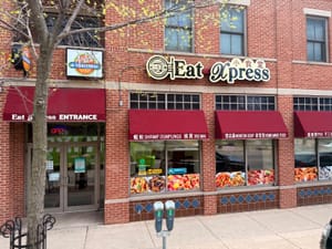 Street view of Eat Xpress restaurant with red awnings, food photos on windows, and a clear entrance sign.