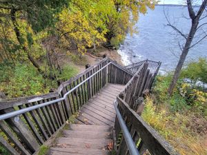 Wooden stairs lead down to a serene lake surrounded by vibrant autumn foliage.
