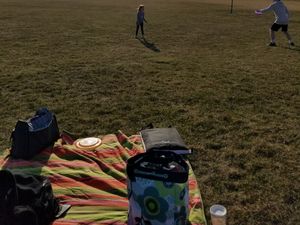 A picnic blanket with bags and a frisbee, children playing in a grassy park.
