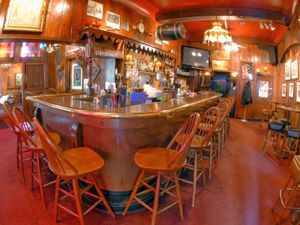 Cozy wood-paneled bar with vintage decor, curved counter, high stools, and warm lighting.