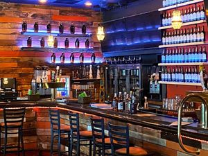 Rustic bar at Third Street Tavern with bottle-lined shelves, glowing lights, and wooden stools.