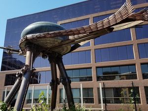 Large whimsical metal insect sculpture with long legs outside Madison Children’s Museum, modern building behind.