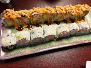 Two sushi rolls on a ceramic plate, one topped with sauce and crispy bits, the other plain with visible crab filling.