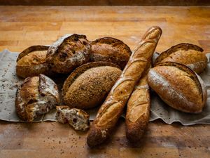 Assorted fresh artisan bread loaves and baguettes on a rustic wooden table with a linen cloth.