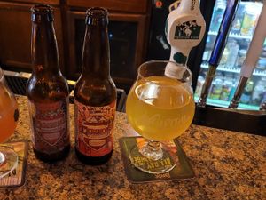Two Mershon’s cider bottles and a glass of golden cider on a bar next to beer taps and a cooler.