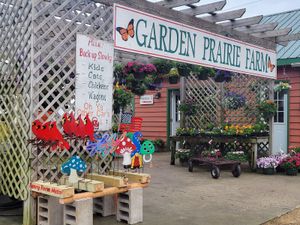 Entrance to Garden Prairie Farm with colorful yard art, potted flowers, and a whimsical welcome sign.