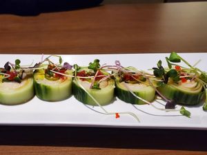 Cucumber-wrapped sushi rolls topped with microgreens and roe on a rectangular white plate.