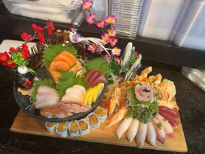 Assorted sashimi, nigiri, and maki rolls artfully arranged with garnishes and decorative flowers on a wooden platter.