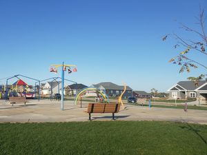 Colorful playground equipment and benches at Nordic Ridge Park with homes in the background on a sunny day.